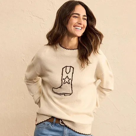 Kremfarget genser med støvel-motiv kombinert med bluejeans.