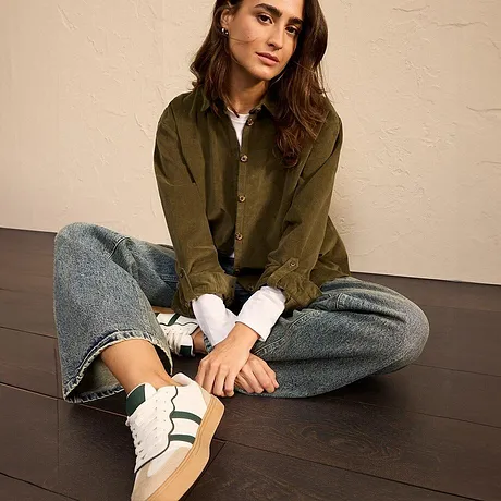 Olivengrønn jakke med jeans og hvite sneakers med grønne striper.