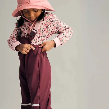 Flerfarget look for barn: Rosa, blomstrete genser, burgunder regnbukse og pastellfarget hatt.
