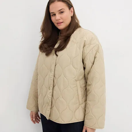 Beige, vattert jakke med knepping kombinert med mørk bukse.
