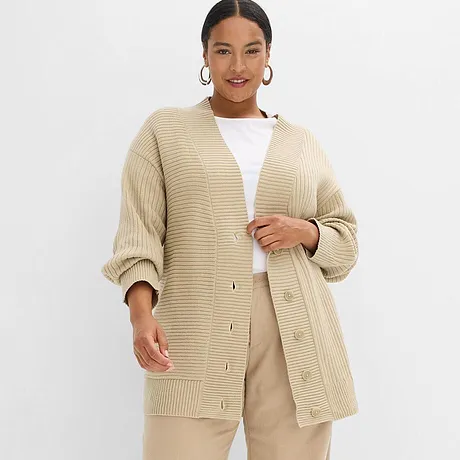 Beige, grovstrikket og oversized cardigan kombinert med hvit topp og lys beige bukse.