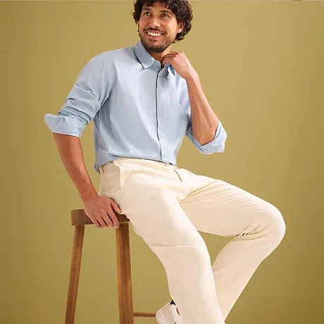 Lyseblå skjorte med oppbrettede ermer, beige dressbukse.