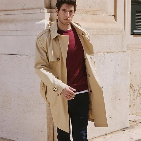 Elegant, beige trenchcoat over rød genser og mørke jeans.