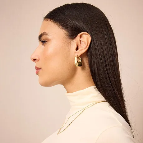 Elegant, kremfarget pologenser, stilren og stilfull. Gullfargede øreringer som eneste smykke.