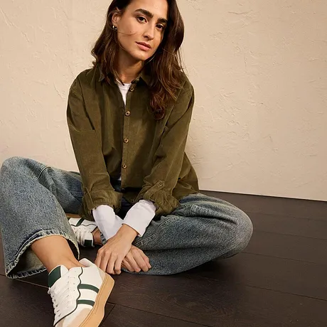 Olivengrønn jakke med jeans og hvite sneakers med grønne striper.