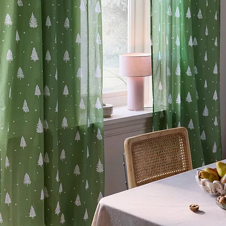 Festlige, grønne gardiner med hvitt juletremønster pynter vinduet.