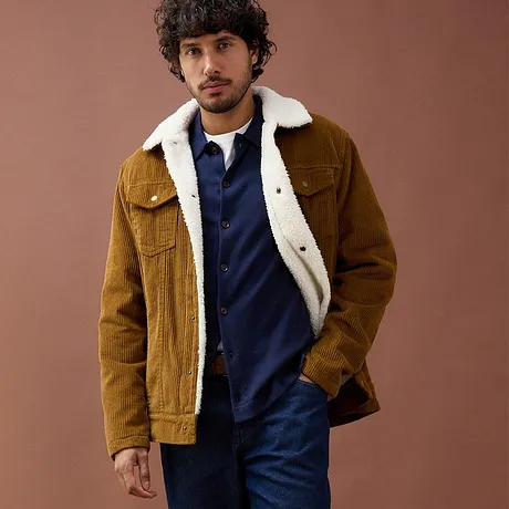 Brun jakke i kordfløyel med lammeskinnskrage over blå genser.