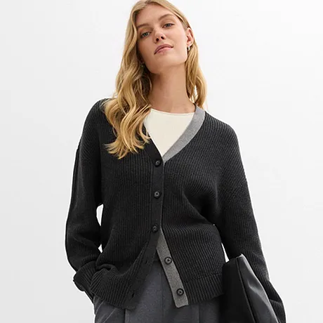 Mørk cardigan over hvit topp kombinert med grått skjørt og sort veske.