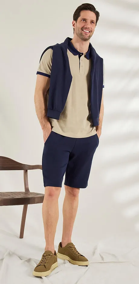 Ledig sommerlook: Beige poloskjorte, mørkeblå vest og shorts, brune sneakers. Avslappet stil.