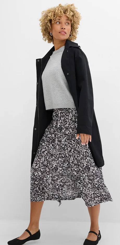 Elegant, sort kåpe, grå topp og langt, mønstret skjørt kombinert med flate sko.