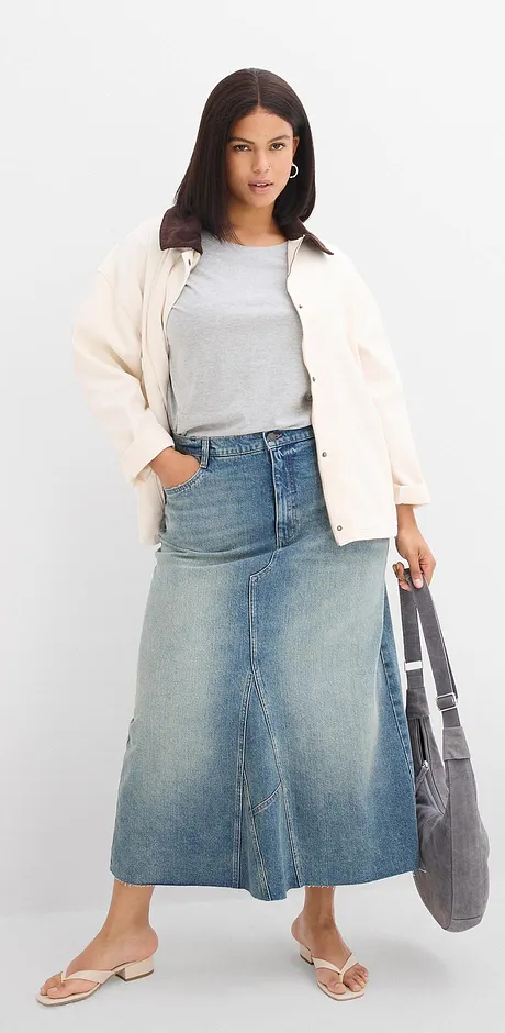 Hvit jakke, grå topp, langt skjørt i denim og behagelige slip in-sandaler.