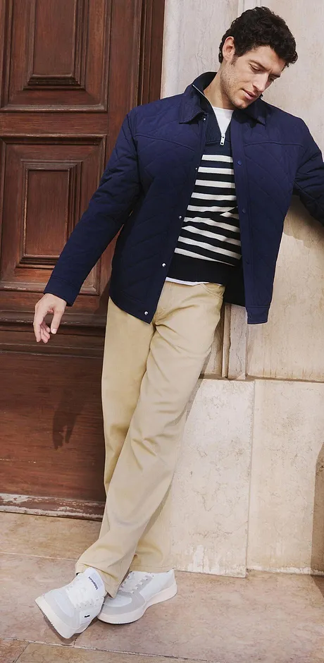 Elegant, mørkeblå jakke over stripete shirt, beige bukse og hvite sneakers.