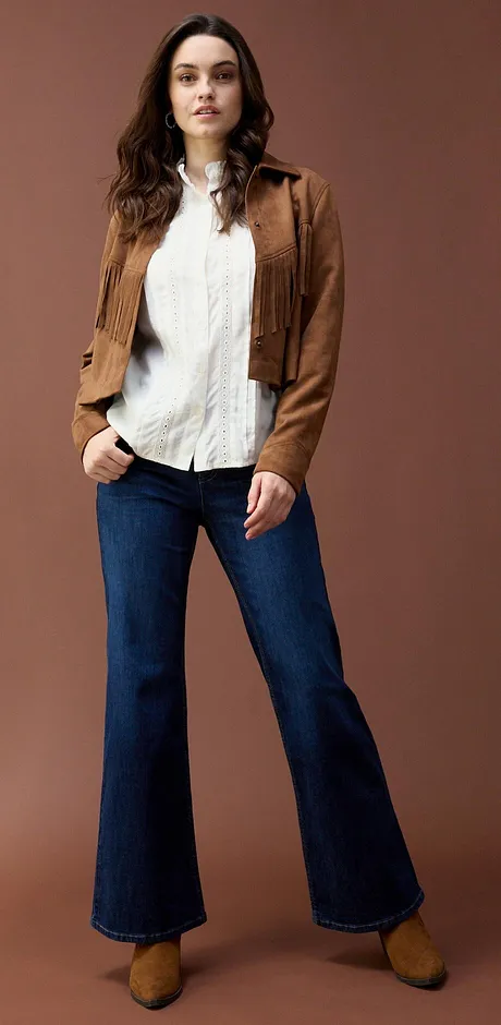 Jakke i semsket skinn over hvit bluse kombinert med utskrådde jeans.