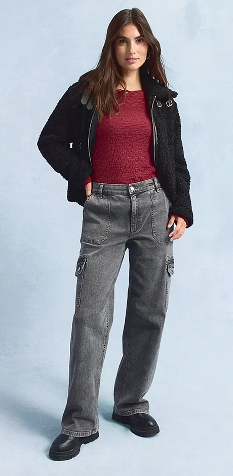 Sort jakke, rød topp, vide, grå jeans og mørke sko.