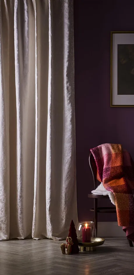 Lyse gardiner pynter vinduet. Et varmt pledd ligger over en stol.