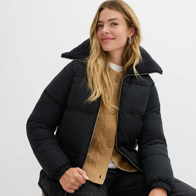 Sort vinterjakke med h&oslash;y krage over gul strikkegenser og hvit topp.