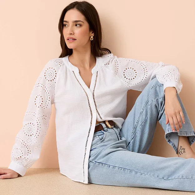 Hvit bluse med hullbroderier og lange ermer kombinert med lysebl&aring; jeans og belte.