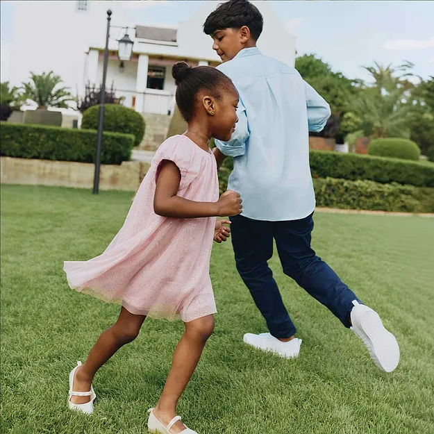 Et barn i rosa kjole danser forn&oslash;yd i hagen.