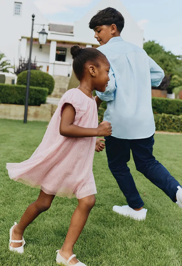 Et barn i rosa kjole danser forn&oslash;yd i hagen.