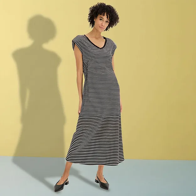 Elegant, sort og hvit stripete kjole med V-hals og sorte sko.