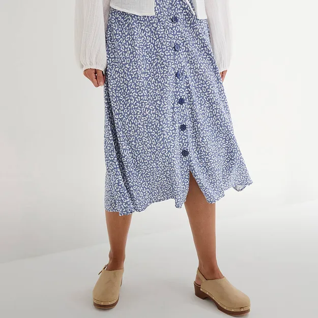 Det bl&aring;, m&oslash;nstrete skj&oslash;rtet med knapper passer perfekt sammen med den hvite blusen og de beige skoene.