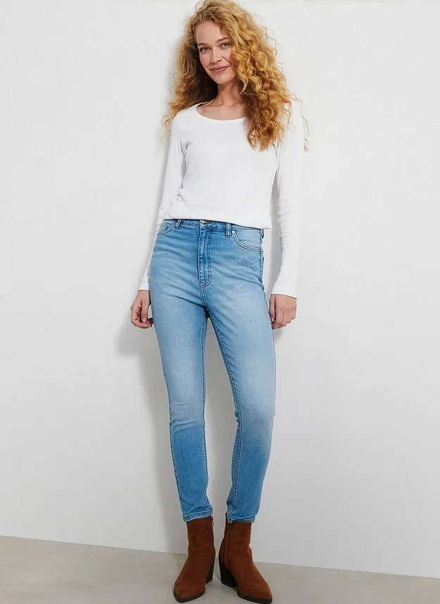 Person i stilren, hvit topp, lyse jeans og brune ankelst&oslash;vletter.
