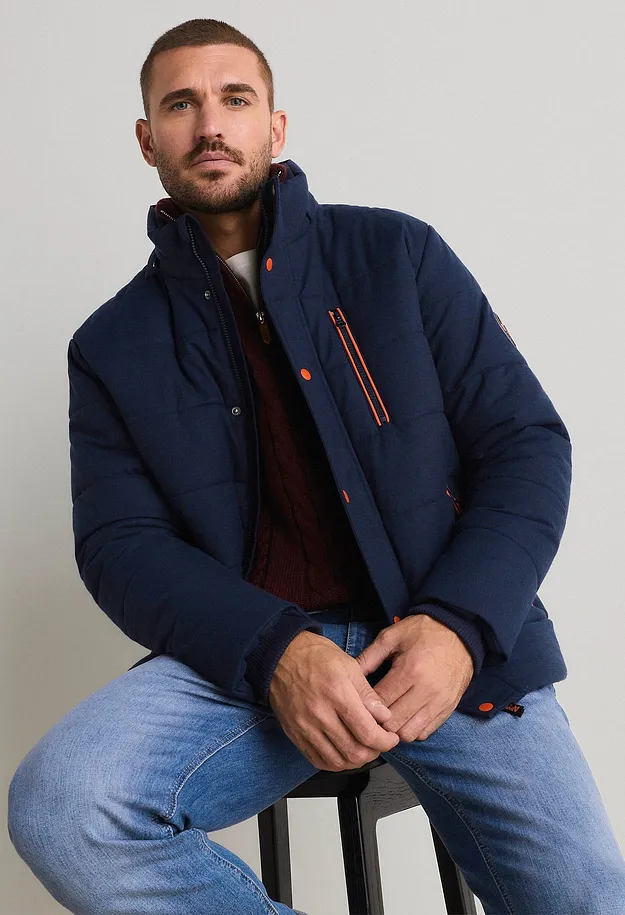 M&oslash;rkebl&aring;, vattert jakke med oransje detaljer, r&oslash;d strikkegenser og lyse jeans.