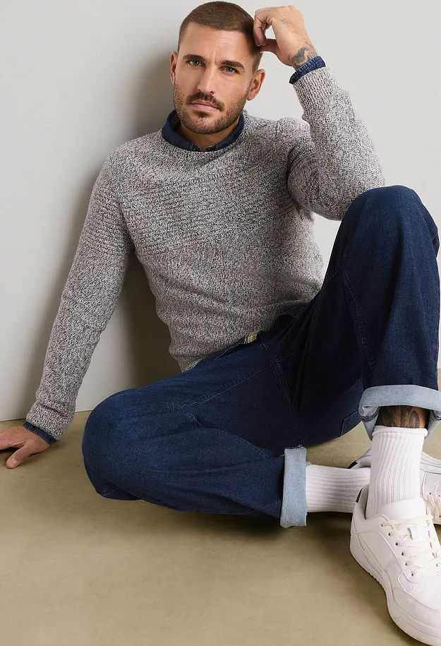 Gr&aring; strikkegenser over bl&aring; skjorte, m&oslash;rke jeans, hvite sokker og sneakers.