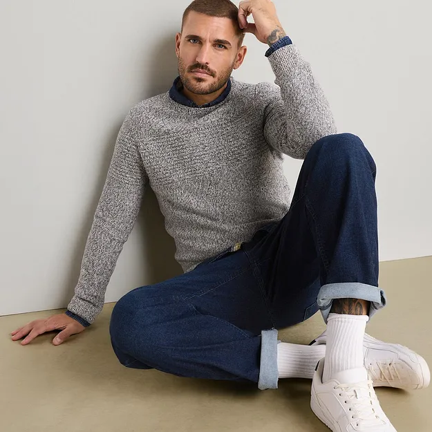 En avslappet og stilig kombinasjon best&aring;ende av strikkegenser i melert garn, bl&aring; skjorte og jeans.