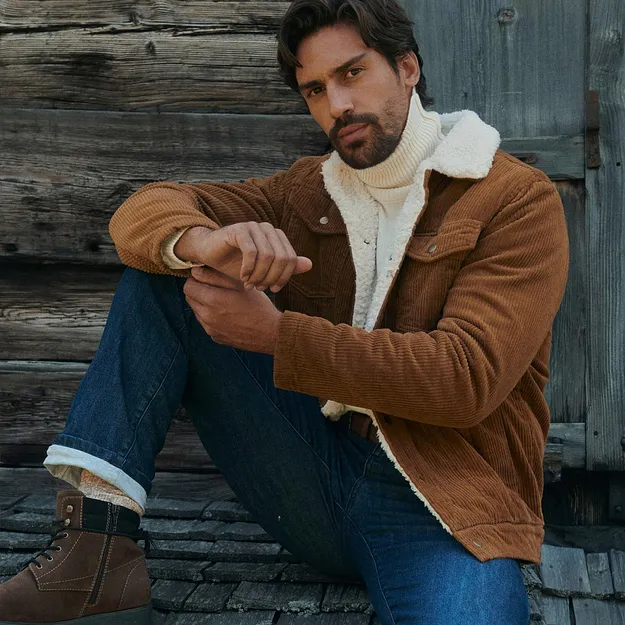 Hen i brun jakke i kordfl&oslash;yel, hvit, h&oslash;yhalset genser, jeans og varme skoletter.
