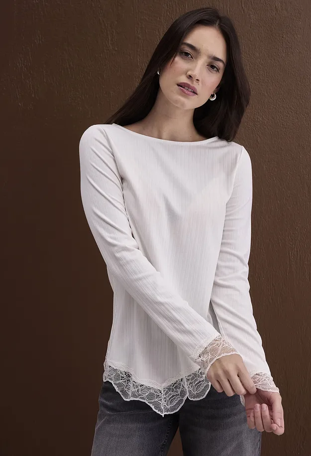 Chic, hvit og langermet topp i ribbemateriale med blonder kombinert med m&oslash;rke jeans.