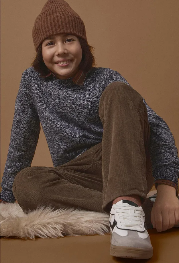 Et barn kledd i brun beanie, rosa genser, bl&aring; jeans og hvite sneakers.