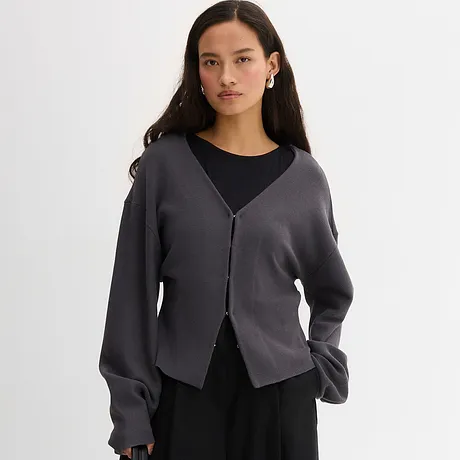Elegant, grå cardigan over en sort topp. Ledig look med V-hals og knappestolpe.