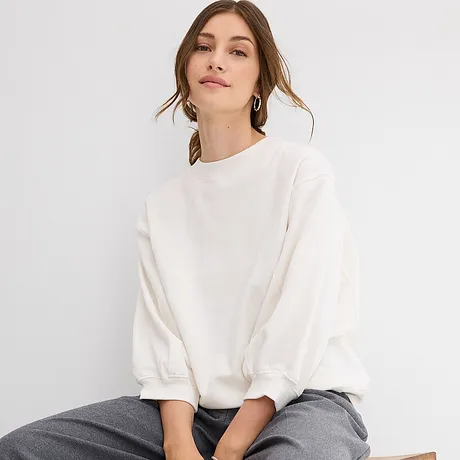 Hvit, oversized sweatshirt med vide ermer kombinert med en grå bukse.
