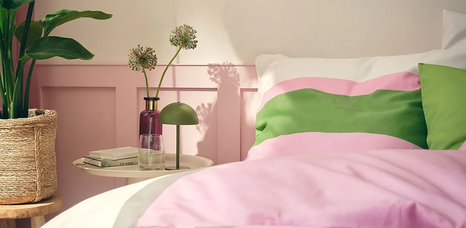 Pastellfarget sengesett i rosa og grønt pynter den behagelige sengen i det solfylte soverommet.