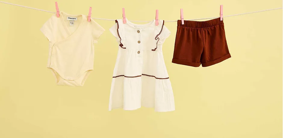 Sommerlige babyklær på klessnoren: Body, hvit kjole og brune shorts til varme dager.