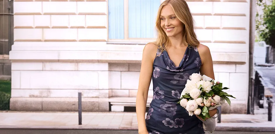 Blå blomstret topp med vannfallsutringning og grå jeans.