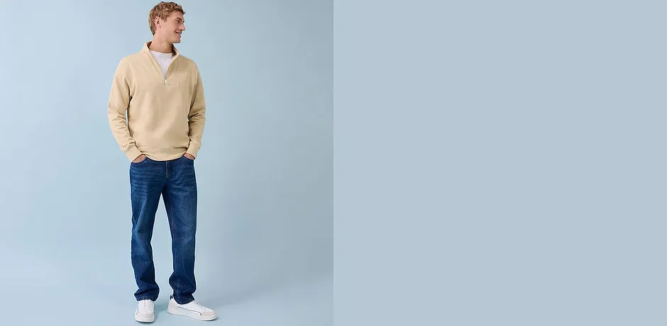 Beige genser med glidelås, blå jeans og hvite sneakers – ledig hverdagslook til han.