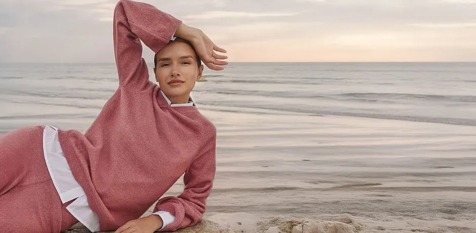 Kvinne i rosa, strikket hettegenser ved havet, behagelig Loungewear-look.