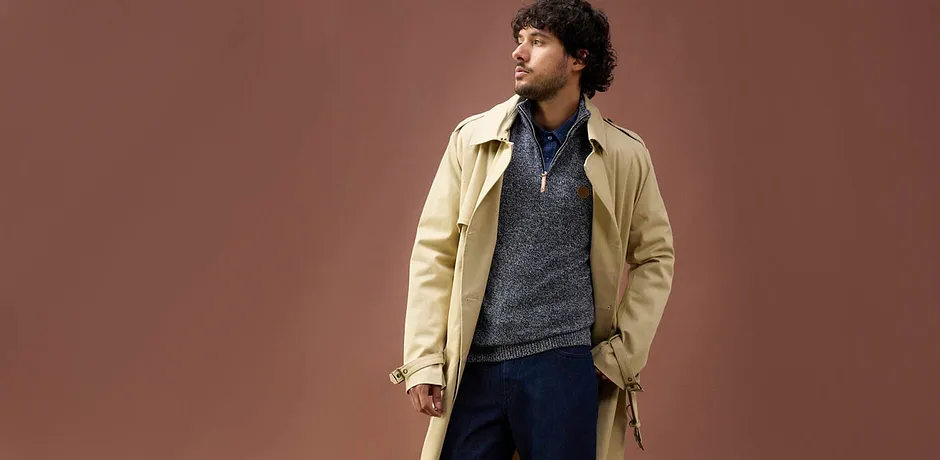 Beige trenchcoat over blågrå, strikket genser og jeans – ledig høstlook for kjølige dager.