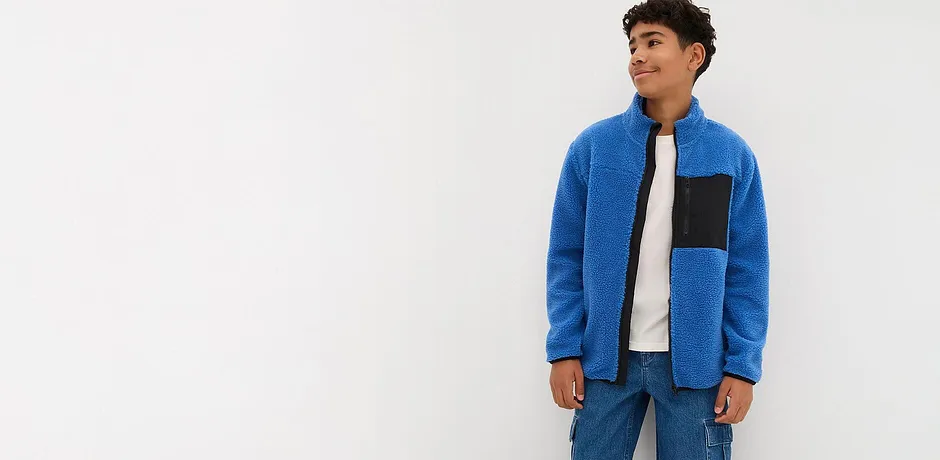 En blå fleecegenser med glidelås og sort innfelling kombinert med jeans og hvit T-skjorte.