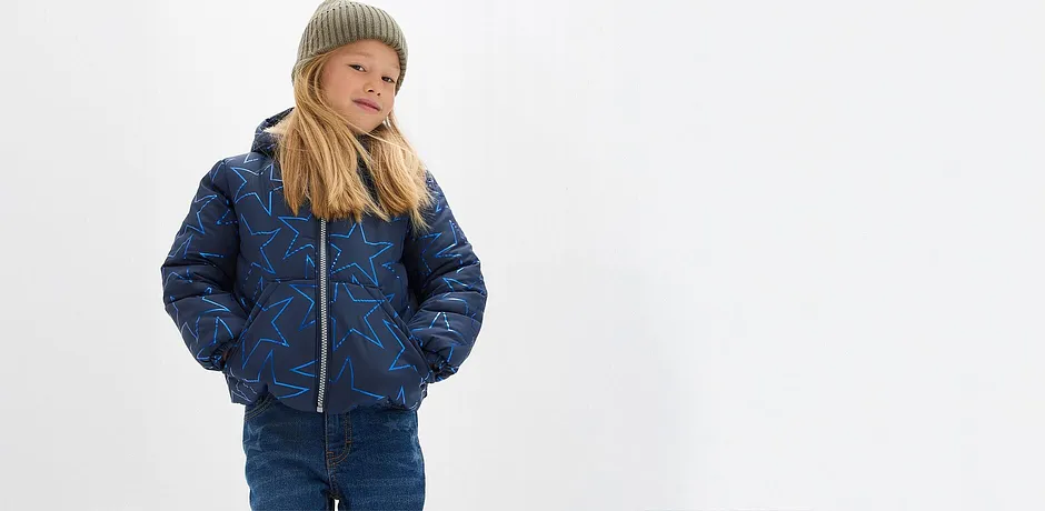 Blå, vattert jakke, jeans og en myk, grønn lue.