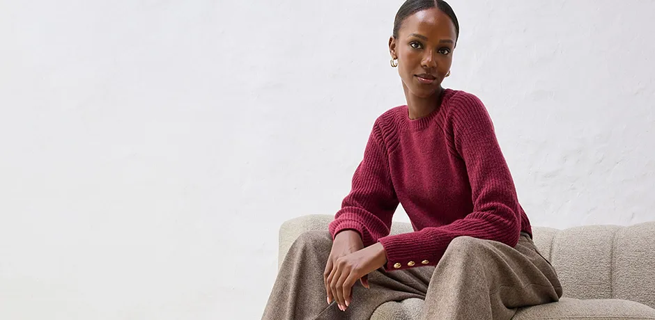 Rød genser med beige bukse på lys sofa.