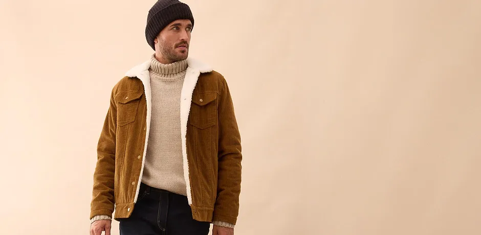 Brun jakke i kordfløyel over kremfarget strikkegenser kombinert med mørke jeans og lue.