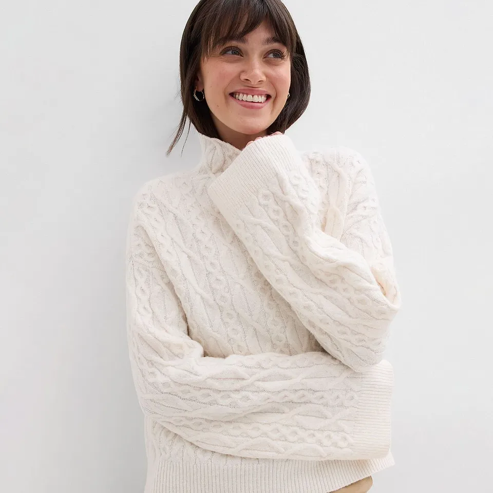 Hvit, kabelstrikket genser med høy krage.