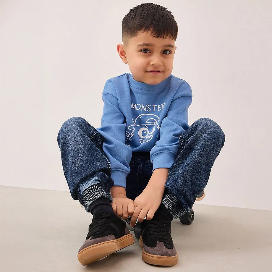 Bl&aring; genser med monster-motiv, m&oslash;rke jeans og sorte sneakers.