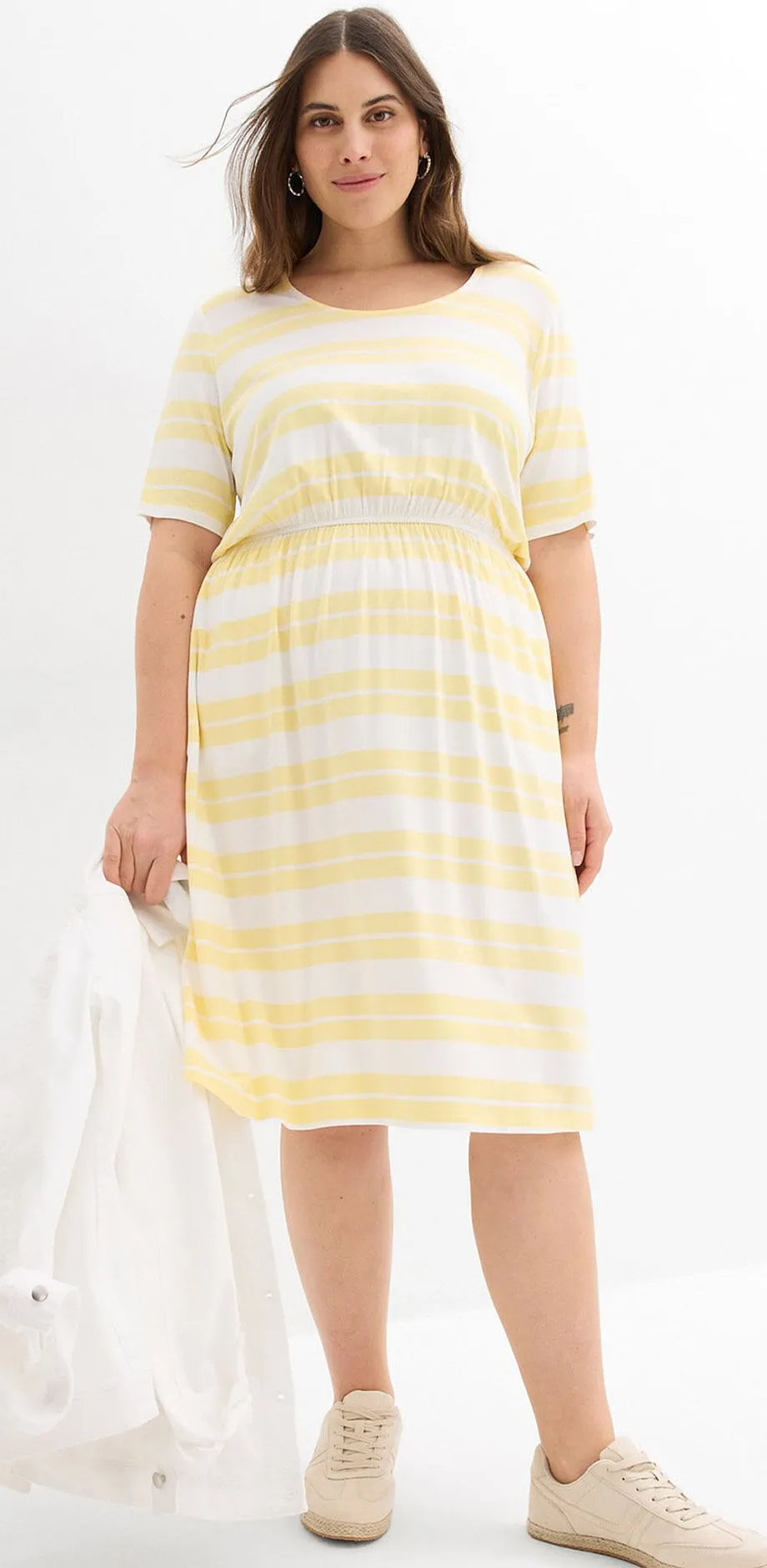 Lysegul, stripete trikotkjole og beige sneakers.