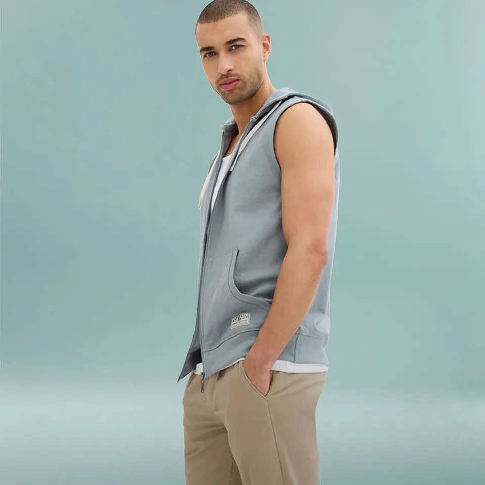 Mann i lysebl&aring; sweatvest med hette, hvit shirt og beige bukse.