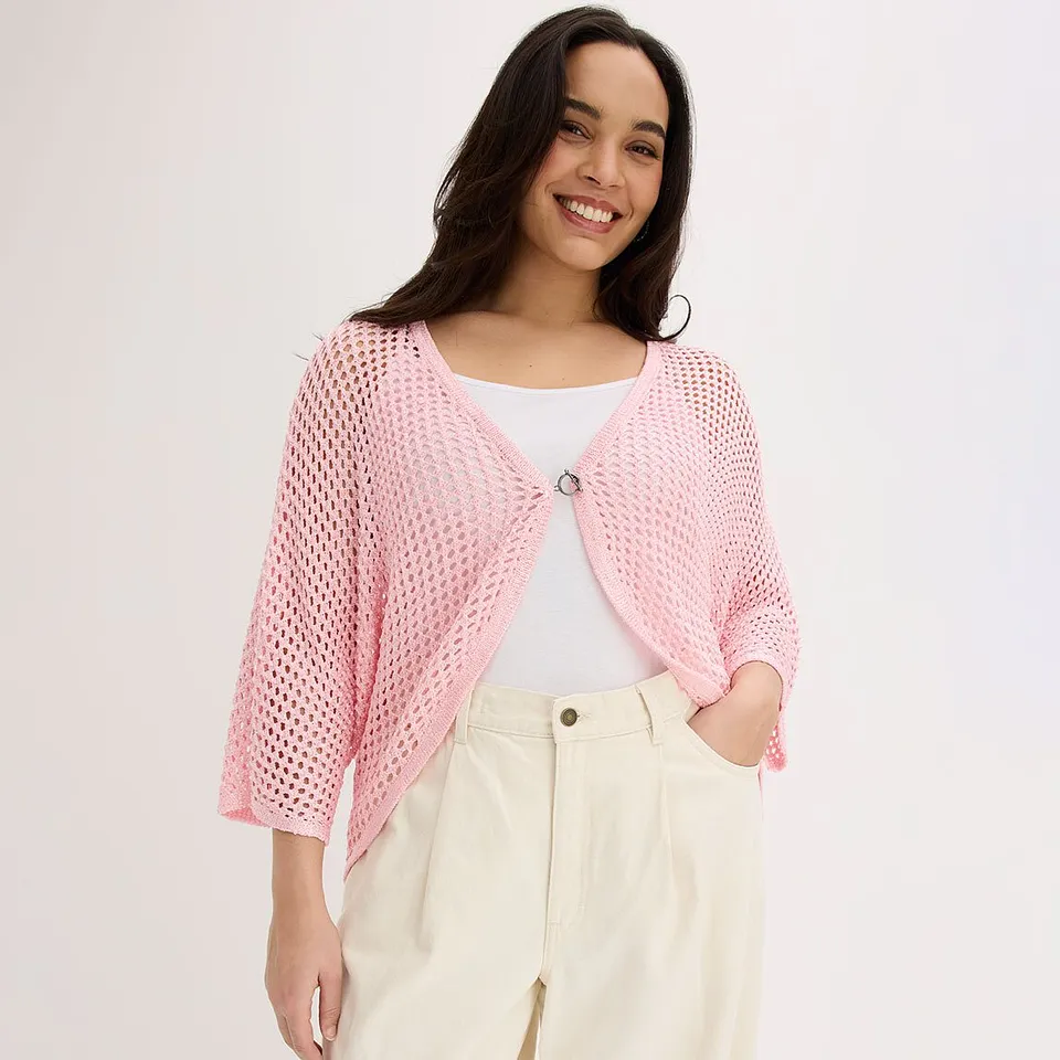 Kvinne i rosa cardigan over hvit topp og kremfarget bukse.