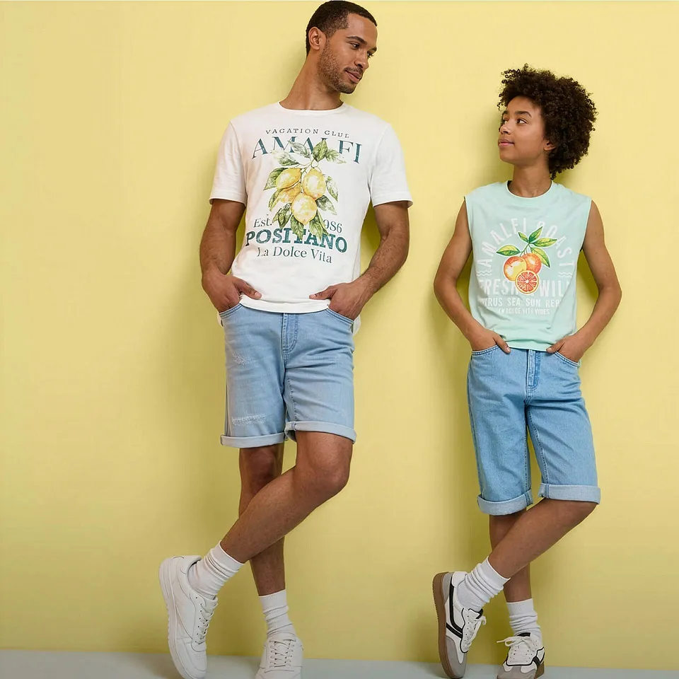To personer i sommerlige outfits med T-skjorter med trykk, denimshorts og hvite sneakers.